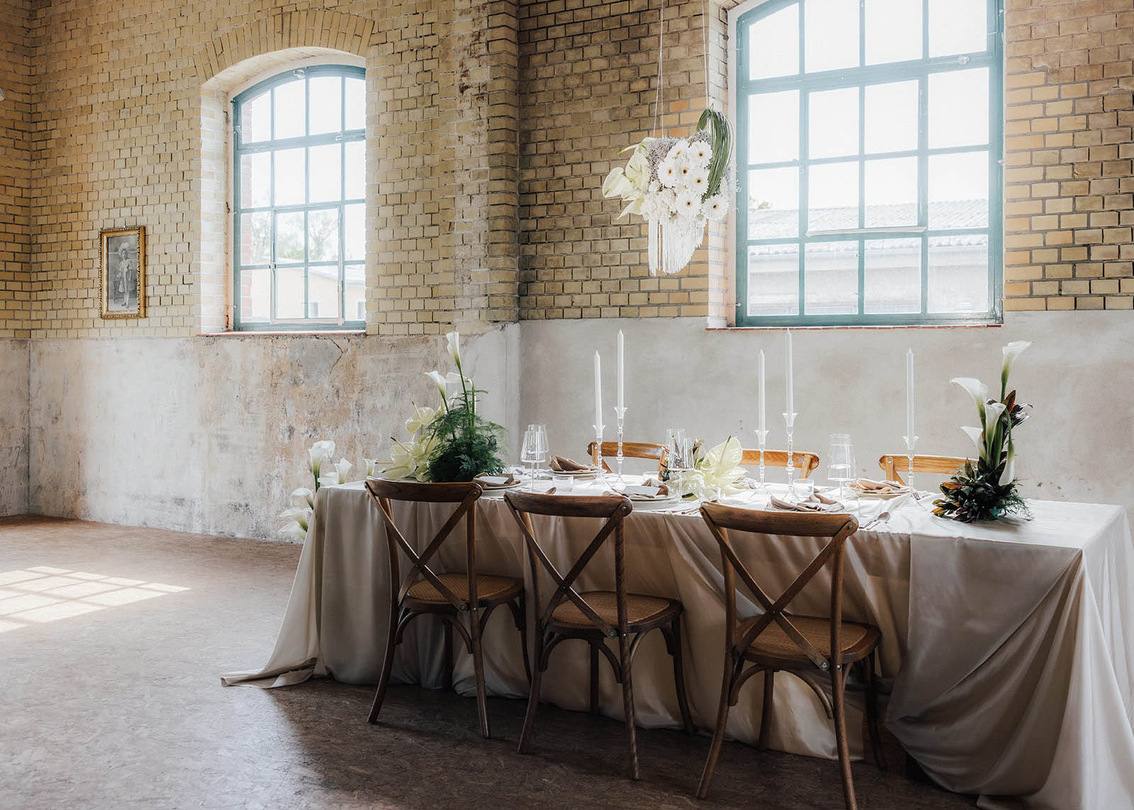 Moderne Hochzeitstafel mit weißer Tischdecke, hohen Stabkerzen, skulpturaler Floristik und schwebender Blumendeko aus Gerbera