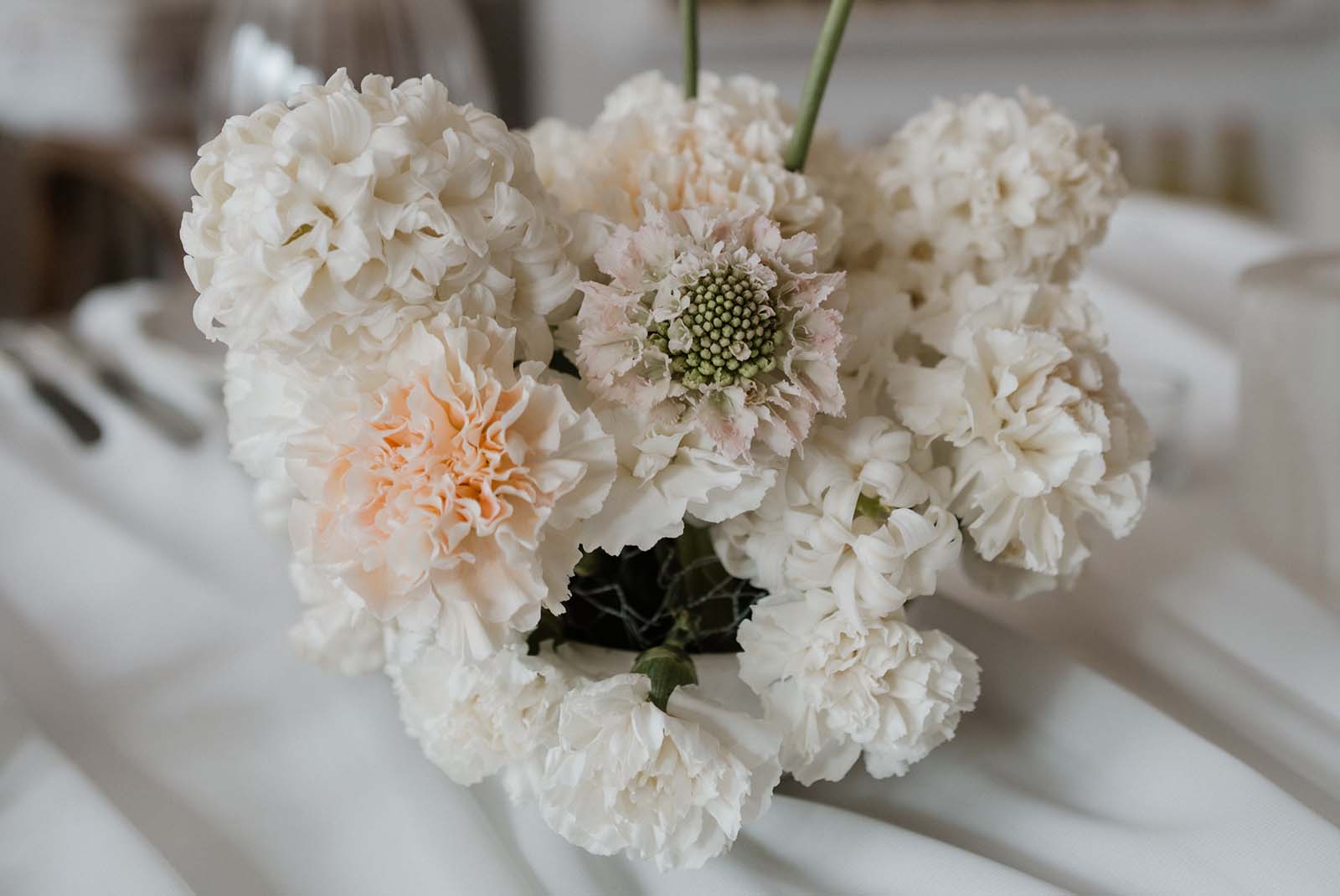 Hochzeitsdeko mit Nelken: Moderne Tischgestaltung mit weißen Nelken, die zu voluminösen Blumenarrangements gesteckt sind.